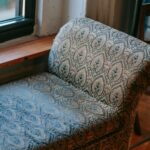 From above of comfortable elegant ottoman bench placed on parquet floor near window in cozy apartment
